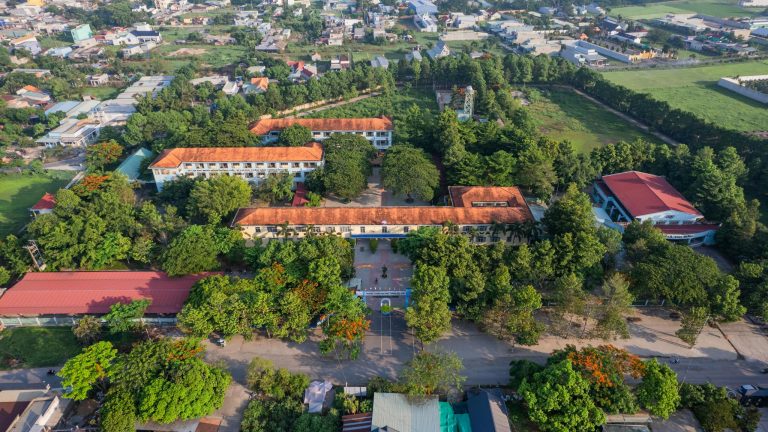 Drone capture of a school campus surrounded by lush greenery and urban development.